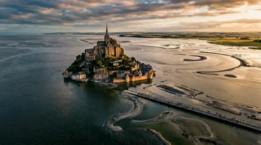 Vue aérienne de la baie du Mont-Saint-Michel lors d'une grande marée, montrant l'eau qui entoure le mont et les parkings submergés