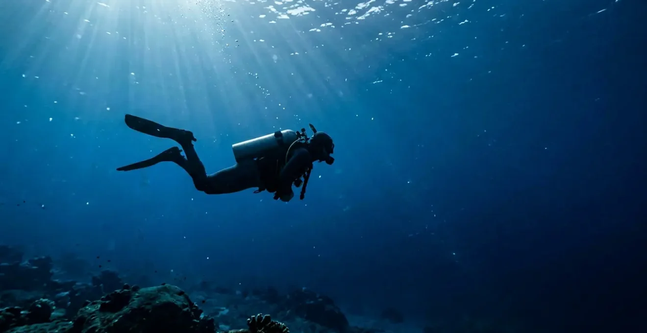 Plongeur en position horizontale parfaite à 20 mètres de profondeur, avec un manomètre visible, entouré de bulles dans une eau cristalline